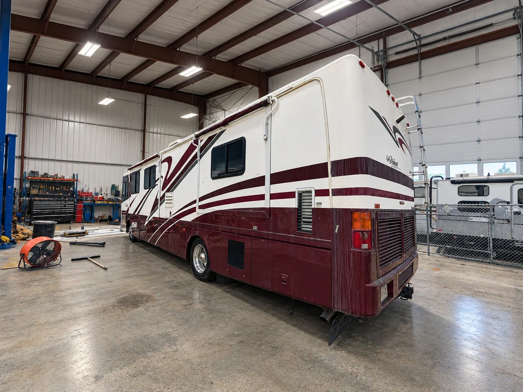 Burgundy and white Class A motorhome in an indoor service bay