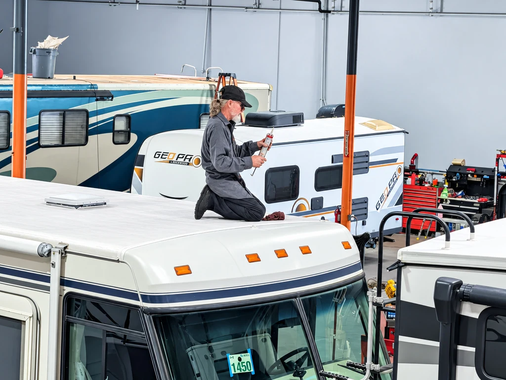 Technician checking roof seals on top of a Class C motorhome at El Toro RV Service