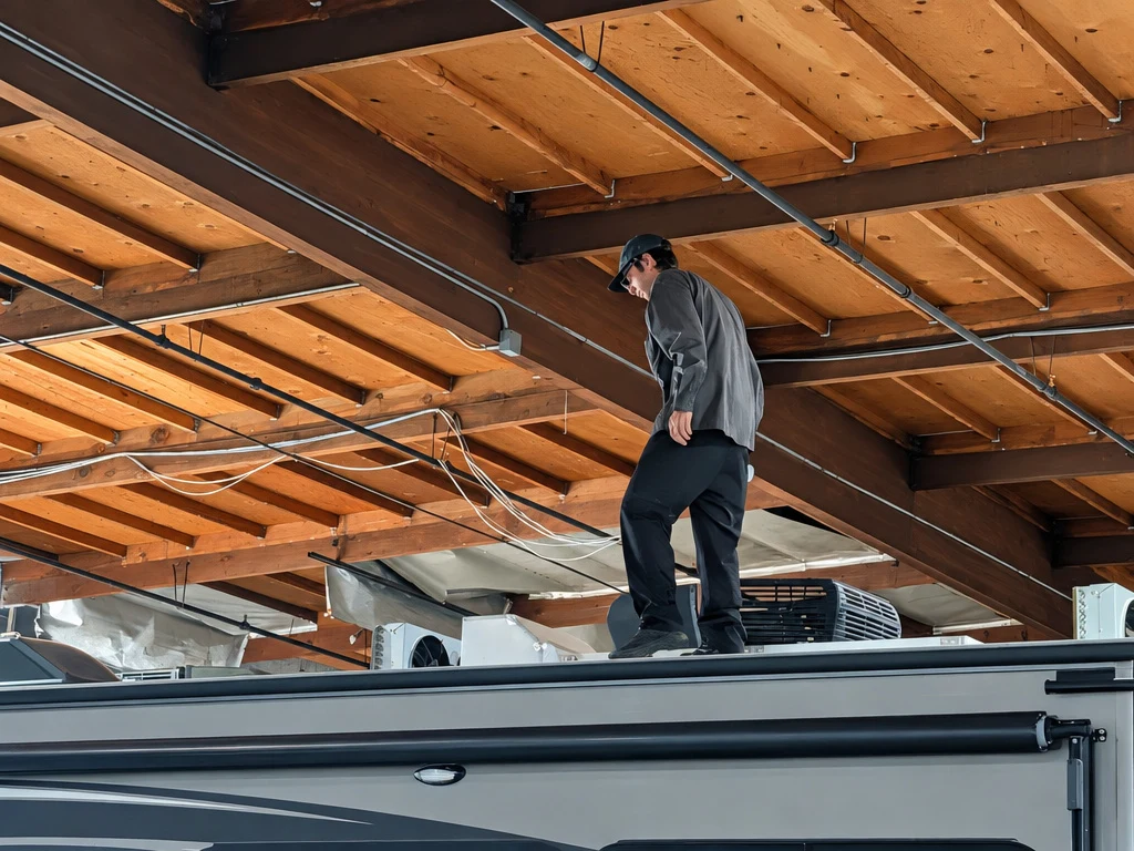 Technician working on top of a tall motorhome inside the El Toro RV shop