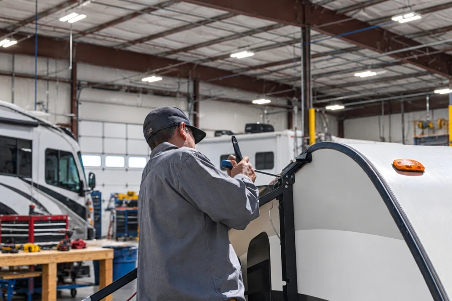 Technician sealing the front cap seam of a travel trailer at El Toro RV Service